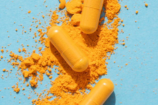 orange curcumin turmeric pills with powder and shadow on blue background