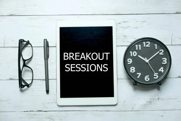 Photo of Business concept. Top view of glasses,pen,clock and tablet written with Breakout Sessions on white wooden background.