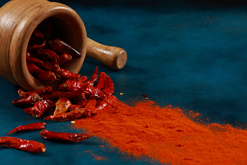 Chilli Peppers and Powder with Mortar and Pestle on a blue stone background