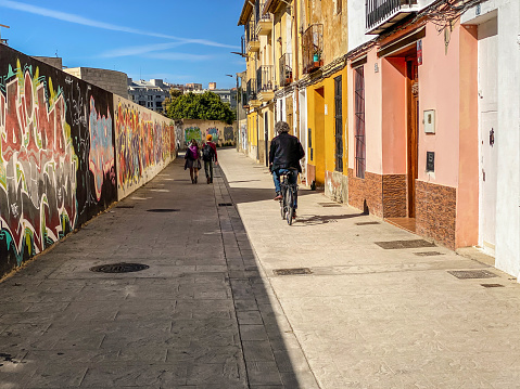 Valencia, Spain - March 22, 2021: Biker and pedestrians crossing colorful alley. There are lots of pedestrian only streets in the city