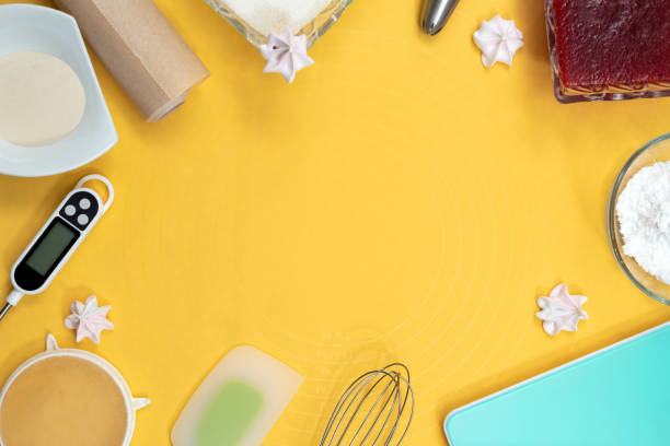 istock Tools and ingredients for making meringue: thermometer, whisk, spatula, parchment, sugar, jam, metal nozzle. Top view. Yellow background with space for text. Selective focus. 1308874955