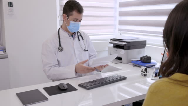 Doctor wearing protective face mask typing report and printing out for patient
