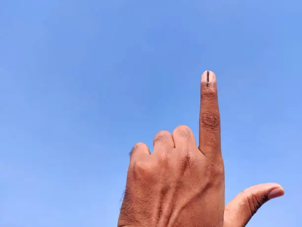 Photo of South Indian man hands with voting sign or inked in forefinger. Cloud background