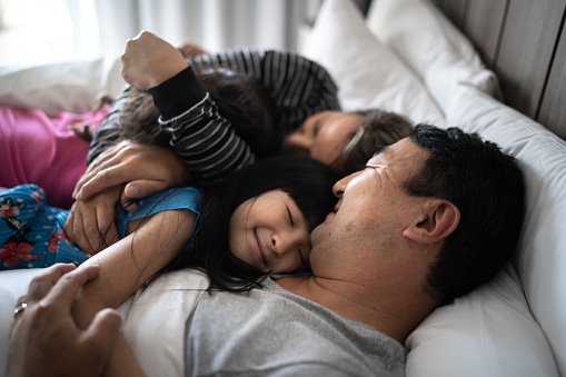 Daughters embracing parents in bed in the morning