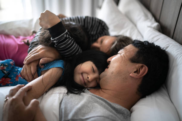 daughters embracing parents in bed in the morning - women common 40s candid imagens e fotografias de stock