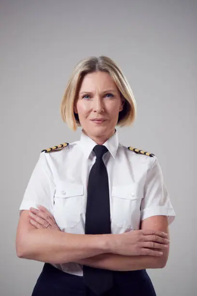 Photo of Studio Portrait Of Smiling Mature Female Airline Pilot Against Plain Background