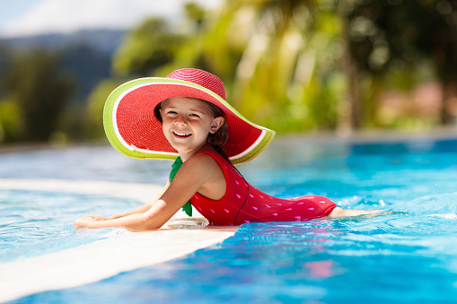 Child in swimming pool. Tropical vacation for family with kids. Little girl wearing red swimsuit and watermelon sun hat playing in outdoor pool of exotic island resort. Water and swim fun for children