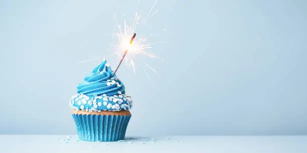 Photo of Blue celebration cupcake with sparkler and sprinkles
