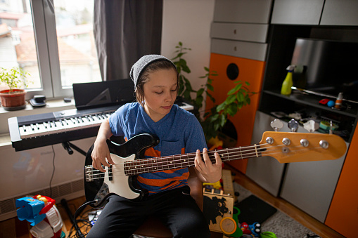 Boy with hat playing guitar in his room.