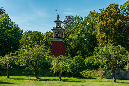 Beautiful summer view of a red wooden clock tower, standing among lush green trees at a closed down silver mine in Sweden