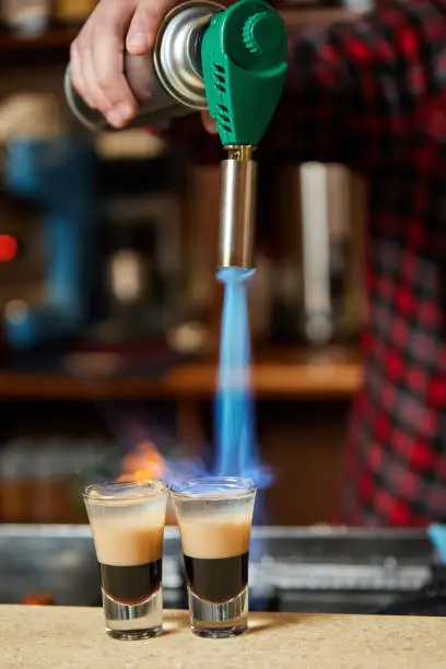 Bartender sets fire the alcoholic drink with gas-burner