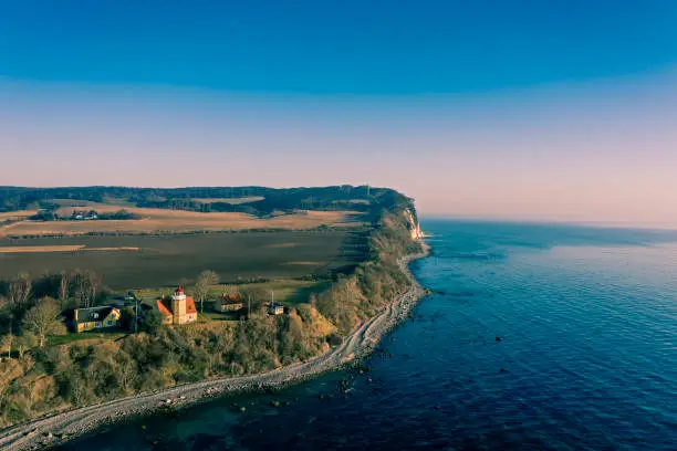 Drone view of the island of Moen in Denmark. Moens Fyr or Lighthouse can be seen in the bottom half of the picture looking out over the Baltic Sea. In the background can be seen the cliffs at Moens Klint. They rise upto 100m high and run for 11 km’s along the Baltic Sea coastline. Colour, horizontal with some copy space.