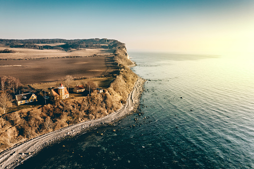 Drone view of the island of Moen in Denmark. Moens Fyr or Lighthouse can be seen in the bottom left of the picture looking out over the Baltic Sea. In the background can be seen the cliffs at Moens Klint. They rise upto 100m high and run for 11 km’s along the Baltic Sea coastline. Colour, horizontal with some copy space.