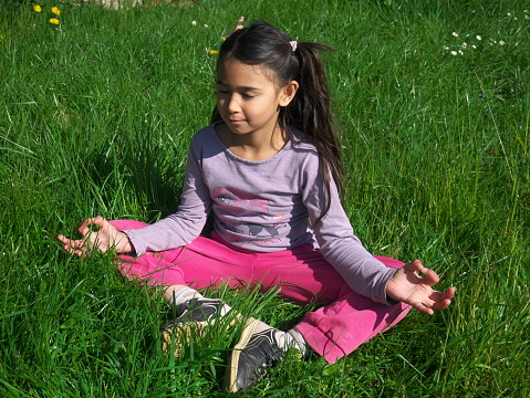 A little mixed-race girl sitting on the grass and meditating.