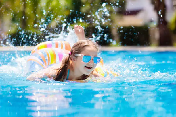 Child with inflatable toy ring float in swimming pool. Little girl learning to swim and dive in outdoor pool of tropical resort. Swimming with kids. Healthy sport activity for children. Water fun.