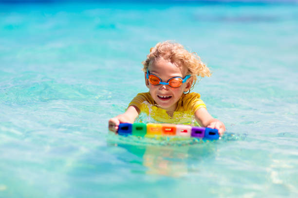 Child surfing on tropical beach. Family summer vacation in Asia. Kids swim in ocean water. Kid on surf body board. Little boy swimming in exotic sea. Travel with children. Water and beach sport.
