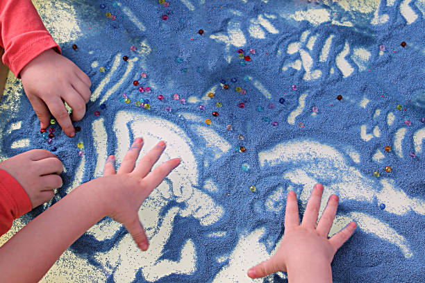 manos de los niños tocando arena azul en la terapia de arena de mesa blanca, desarrollo de habilidades motoras finas - sandbox child human hand sand fotografías e imágenes de stock