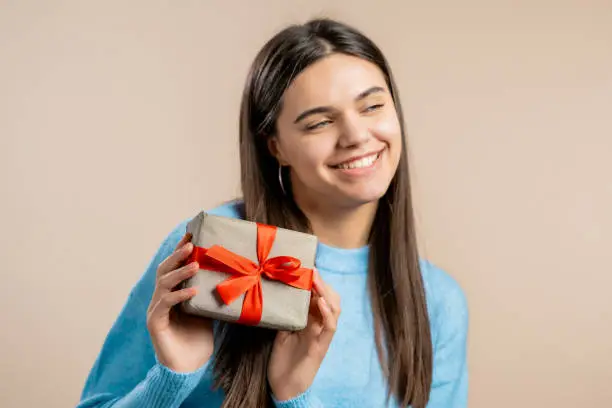 Excited woman received gift box with bow. She is happy and flattered by attention. Girl smiling with present on light background. Studio portrait.
