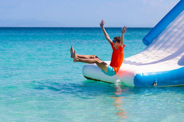 Kids on trampoline on tropical sea beach. Kids jumping on trampoline on tropical sea beach. Children jump on inflatable water slide. Aqua amusement park in exotic island resort. Family vacation and travel with child. Ocean coast fun. sliding down stock pictures, royalty-free photos & images