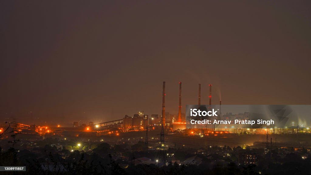Night urban landscape with an industrial complex Night urban landscape with an industrial complex with its metal structures and chimneys with reflection of lamps with yellow lights of the city. India Stock Photo