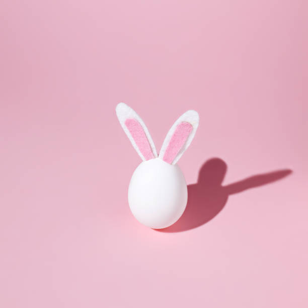 istock White egg with fluffy bunny ears and summer shadow on pastel pink background 1308911946