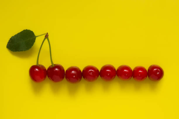 istock Ripe red cherries with a handle and a leaf lie on a yellow background. Place for text 1308913221