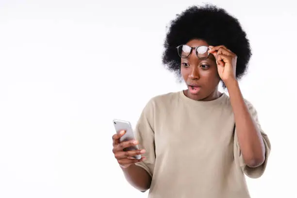 Shocked african teenage girl using cellphone emotionally isolated over white background