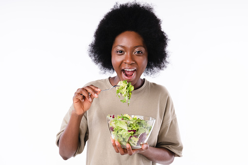Hungry african teen girl eating salad isolated over white background