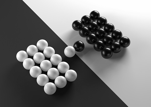 Conceptual illustration of two arrangements of black and white spheres facing each other, with strong contrast.