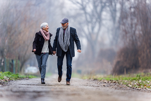 Cheerful mature couple having fun while holding hands and running in nature. Copy space.
