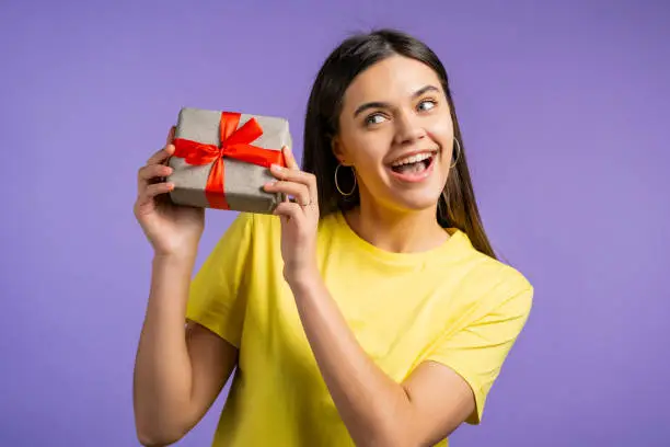 Beautiful woman received gift box with bow. She is happy and flattered by attention. Girl smiling with present on violet background. Studio portrait.