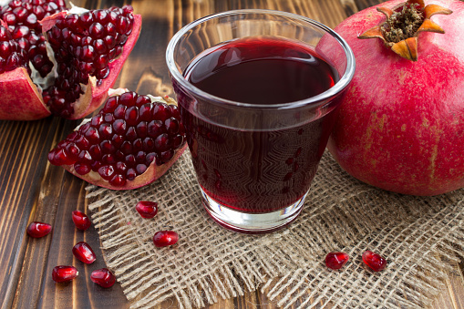 Pomegranate juice in the drinking glass on the wooden rustic background. Close-up.