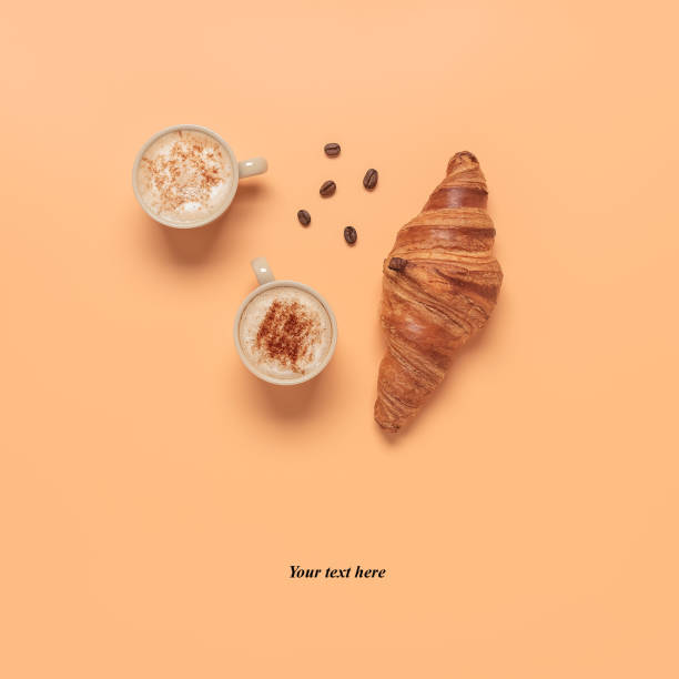 istock Coffee cups and fresh croissant on a pastel peach color background. Creative layout. Breakfast concept. Top view, flat lay. 1308922549