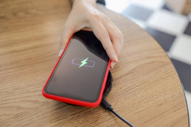 istock Charging mobile phone battery with wireless device in the table. Smartphone charging on a charging pad. Mobile phone near wireless charger. 1308923489