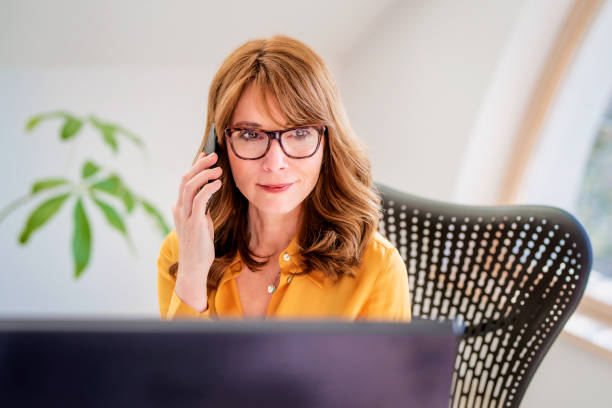 istock Businesswoman using mobile phone and computer while working from home 1308923877