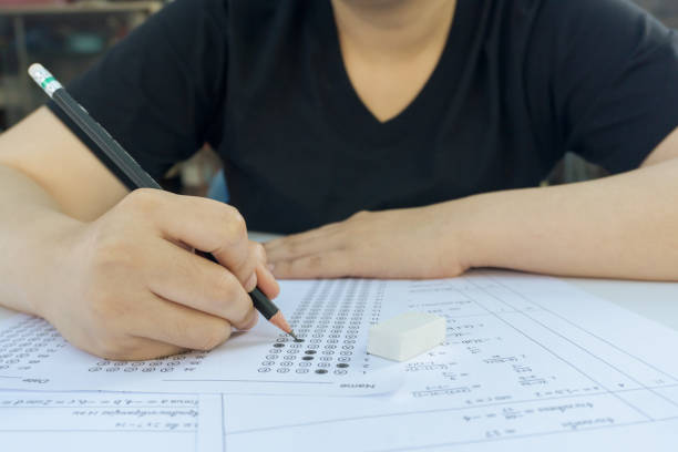 istock Woman students hand holding pencil writing selected choice on answer sheets and Mathematics question sheets. students testing doing examination. school exam 1308927263