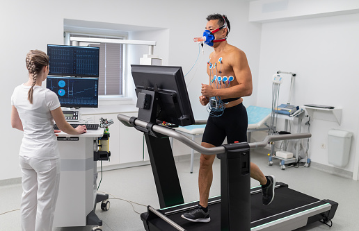 Young adult man having a VO2 test with a VO2 mask on his face, electrocardiogram pads attached, treadmill