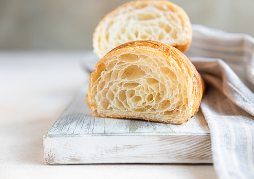 Cut in half croissant with inside texture and thin crisp layers on wooden board, light concrete background. Delicious french pastry. Selective focus.