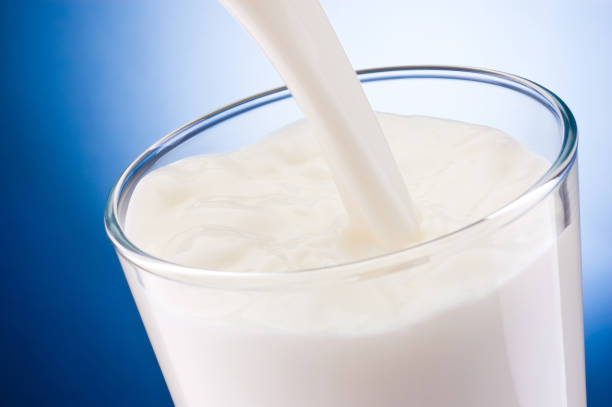 istock Milk poured into glass on blue background 1308936148