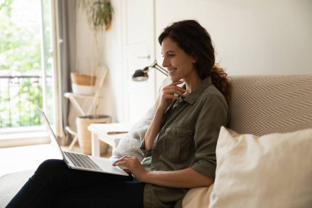 istock Smiling millennial female sit on couch hold laptop chat online 1308937474