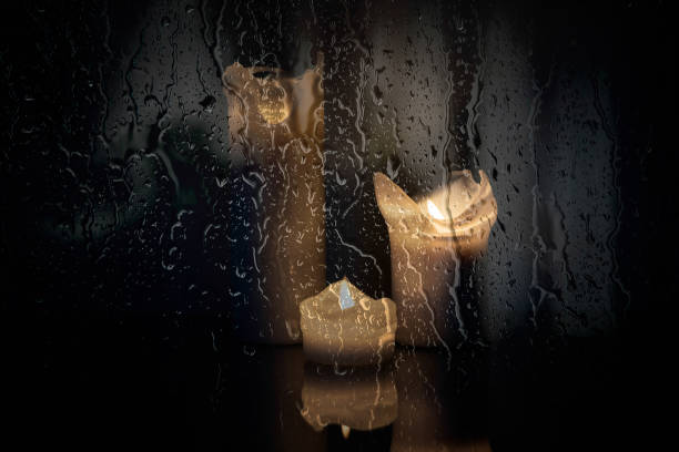 Three lit candles behind a wet window glass