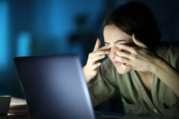 Fatigued woman with eyestrain using laptop in the night