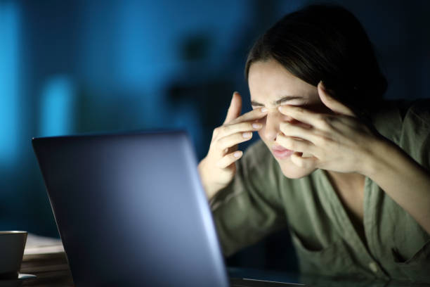 fatigued woman with eyestrain using laptop in the night - effort dark concepts women imagens e fotografias de stock