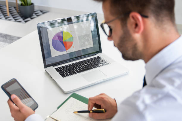 istock Businessman sitting at desk and using mobile phone and laptop while working in the office 1308942637