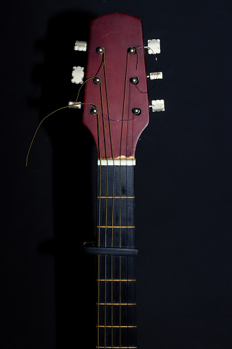 Guitar head and neck and capo on a black background. Wooden acoustic six-string guitar.