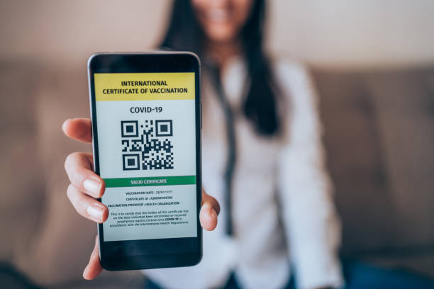 Digital Immunization Certificate. Defocused young woman showing smartphone with valid digital international vaccination certificate for COVID-19. Focus is on the smart phone. vaccine passport photos stock pictures, royalty-free photos & images