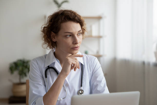 istock Pensive female doctor work on laptop thinking 1308949148