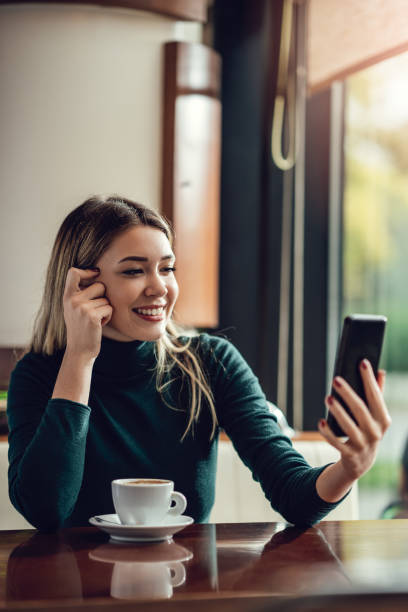 istock Young happy woman at restaurant drinking coffee and using mobile phone. 1308952006