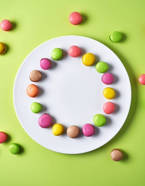 Various colored mini macarons on white plate and light green background, top view
