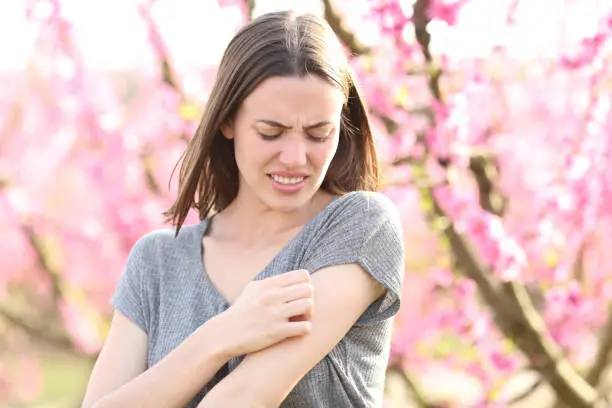 Photo of Stressed woman scratching itchy arm after insect bite in a field